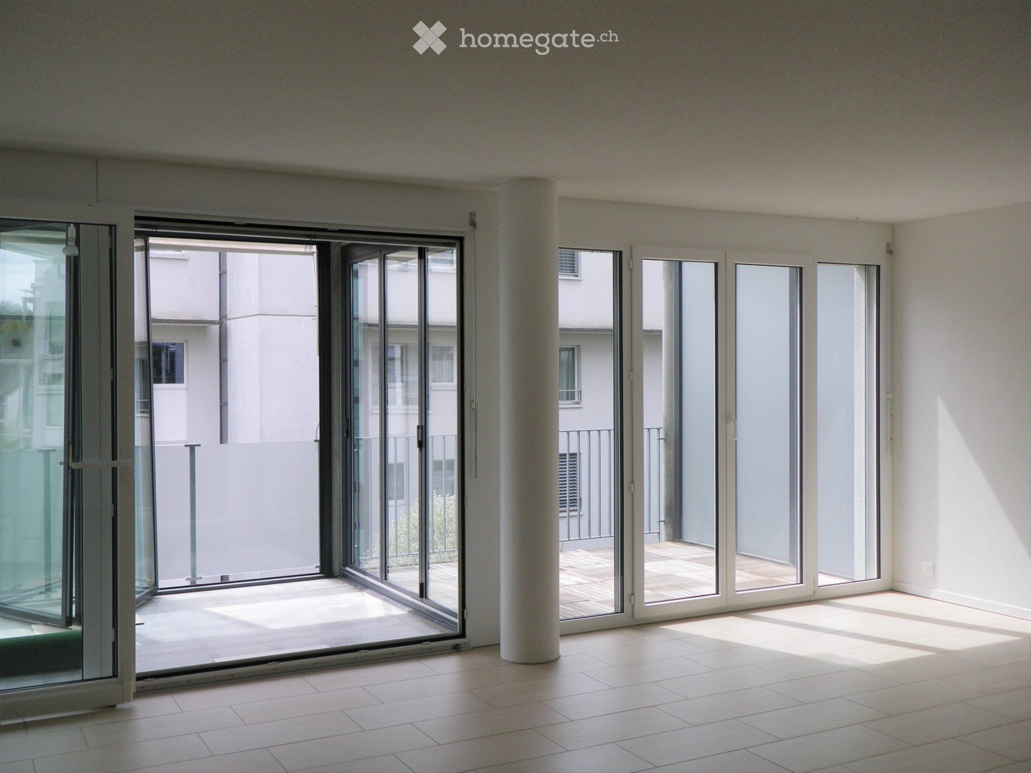 Empty room with large sliding glass doors leading to a balcony area, tiled floor, and white walls.