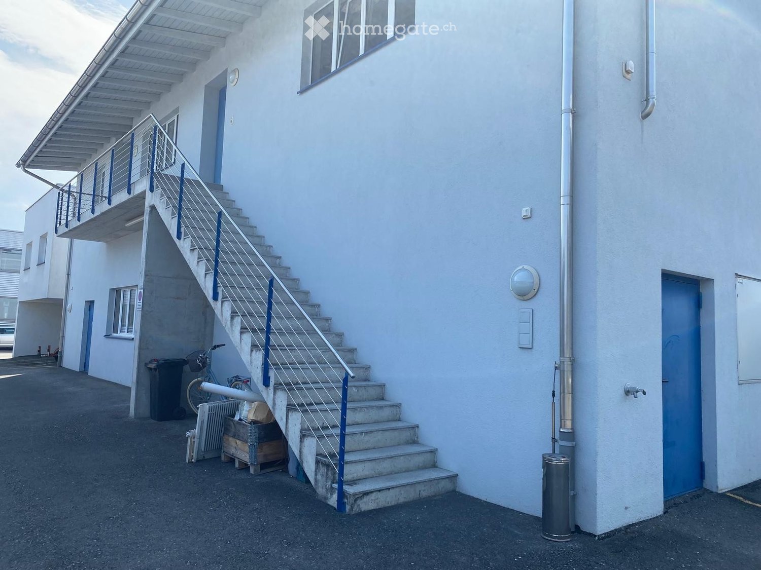 Exterior view of a two-story building with a staircase leading to an upper level, featuring a metal railing and blue doors.