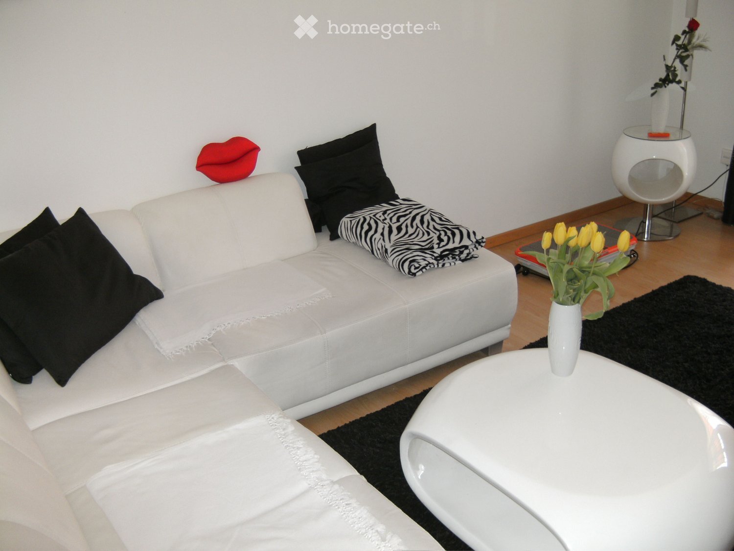Modern living room with white leather sofa, black pillows, zebra throw, white coffee table, vase with yellow tulips, and a round white stool.