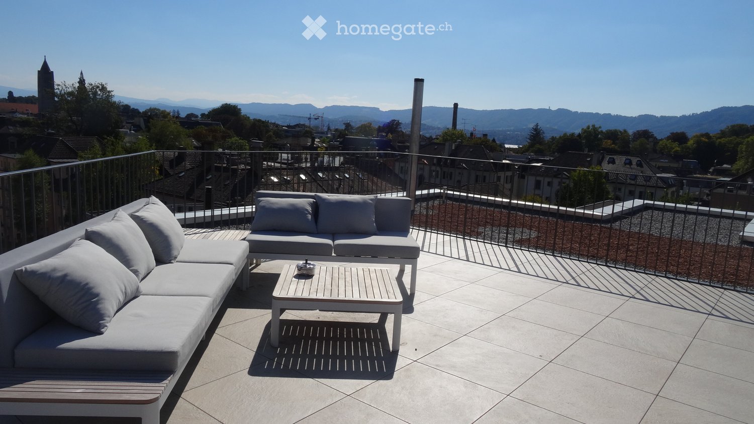Modern rooftop terrace with white sofas, coffee table, and scenic city view.