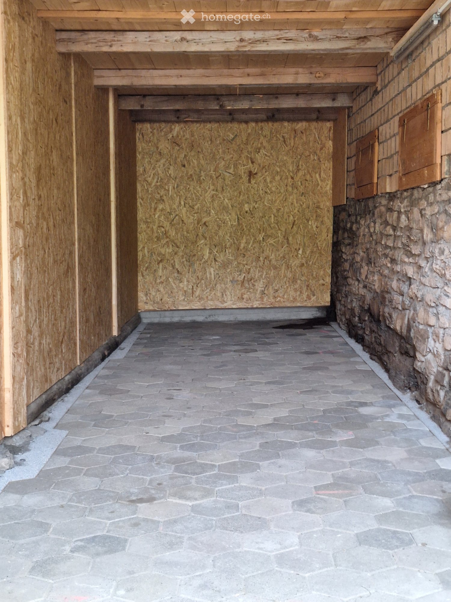 Empty hallway with hexagonal stone tiles, wooden paneling on one side, and stone wall on the other.