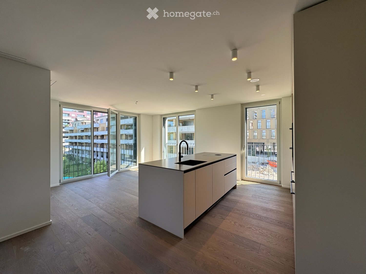 Modern kitchen with light wood flooring, white cabinetry, island with sink, and large windows overlooking a cityscape.