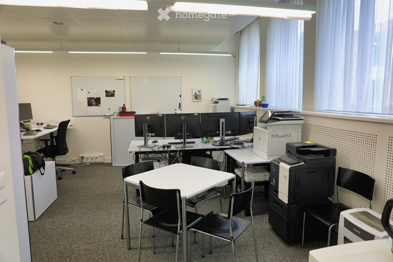 An office with desks, chairs, whiteboards, printers, and office equipment.