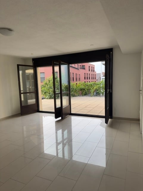Empty room with large sliding glass doors leading to an outdoor area, tiled floor, and neutral-colored walls.