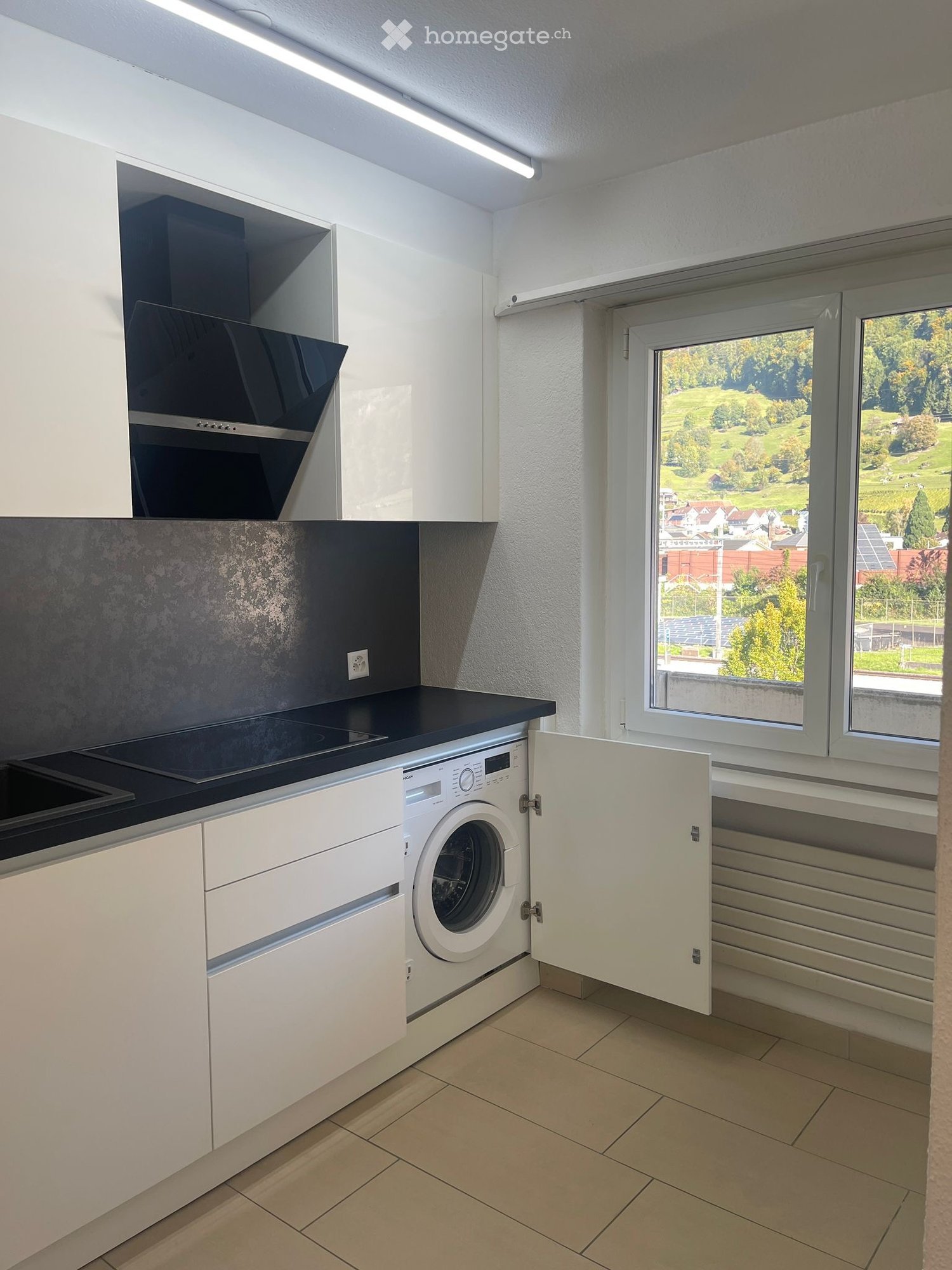 modern kitchen with white cabinets, black countertops, modern washer, and large window with view
