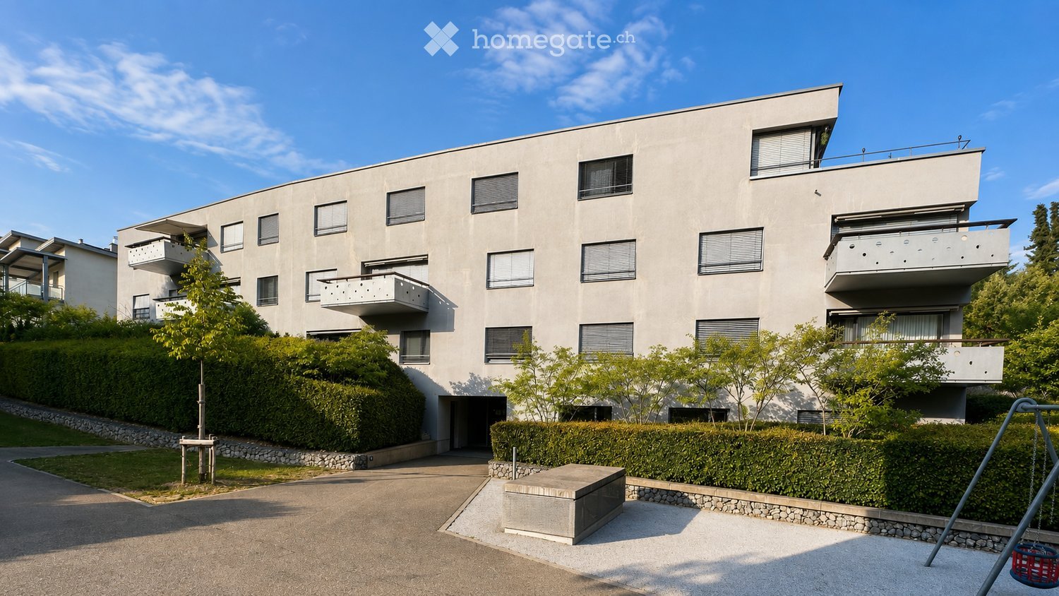 Modern multi-story residential building with balconies, surrounded by greenery and a small playground area.
