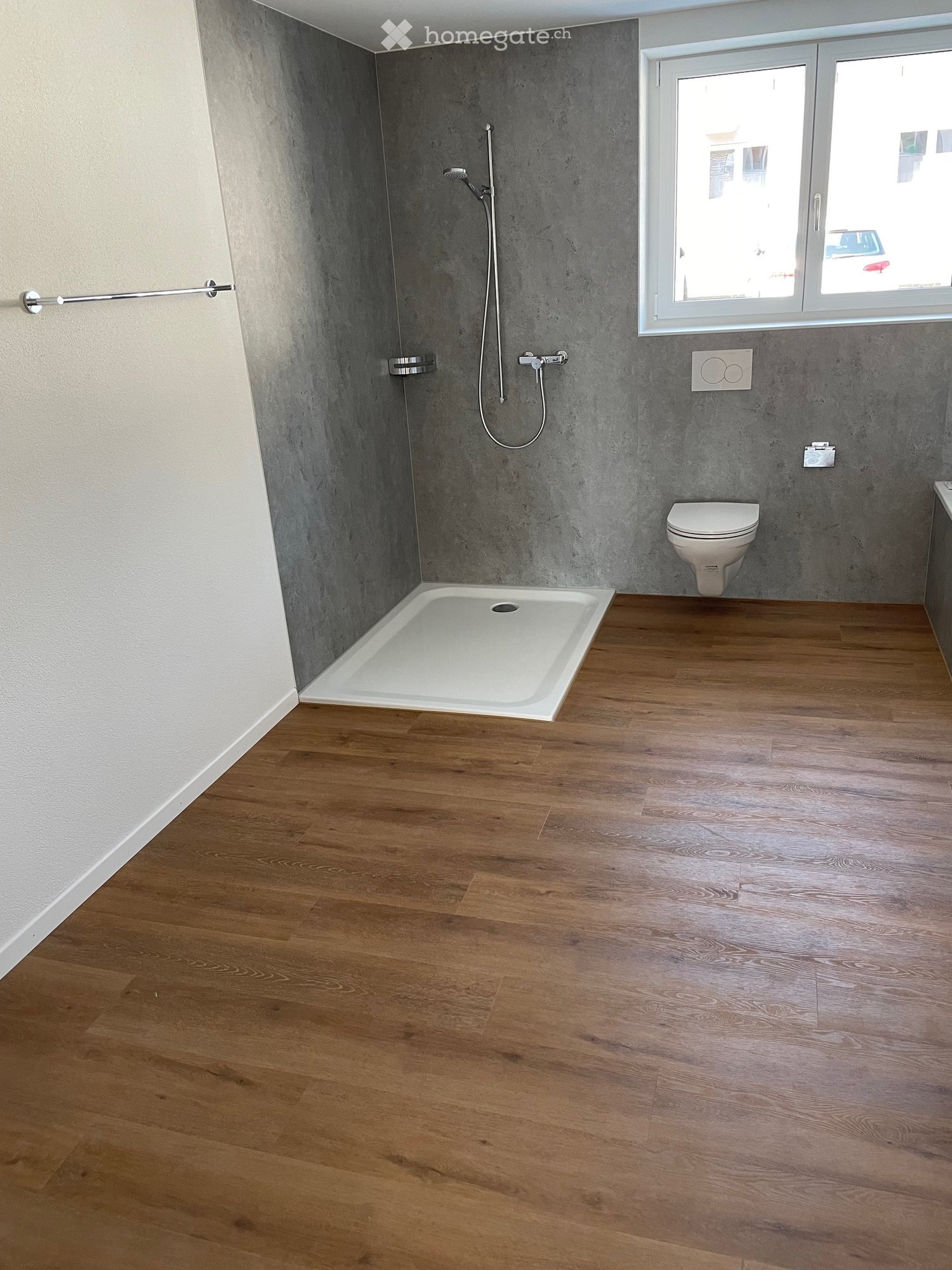 Modern bathroom with wooden flooring, a bathtub, toilet, and a shower area with grey tiled walls.