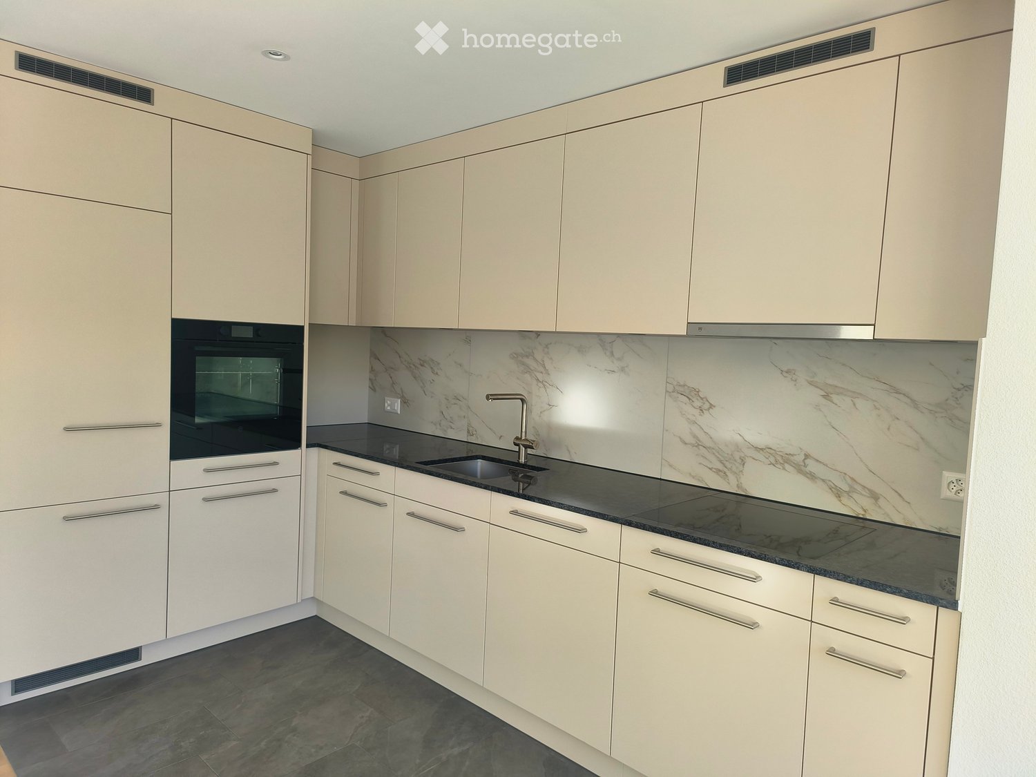 Modern kitchen with light-colored cabinets, marble backsplash, black countertop, and stainless steel sink and faucet.