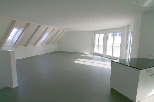 Bright, open room with large windows and skylights, featuring a kitchen area with a counter and cabinets.
