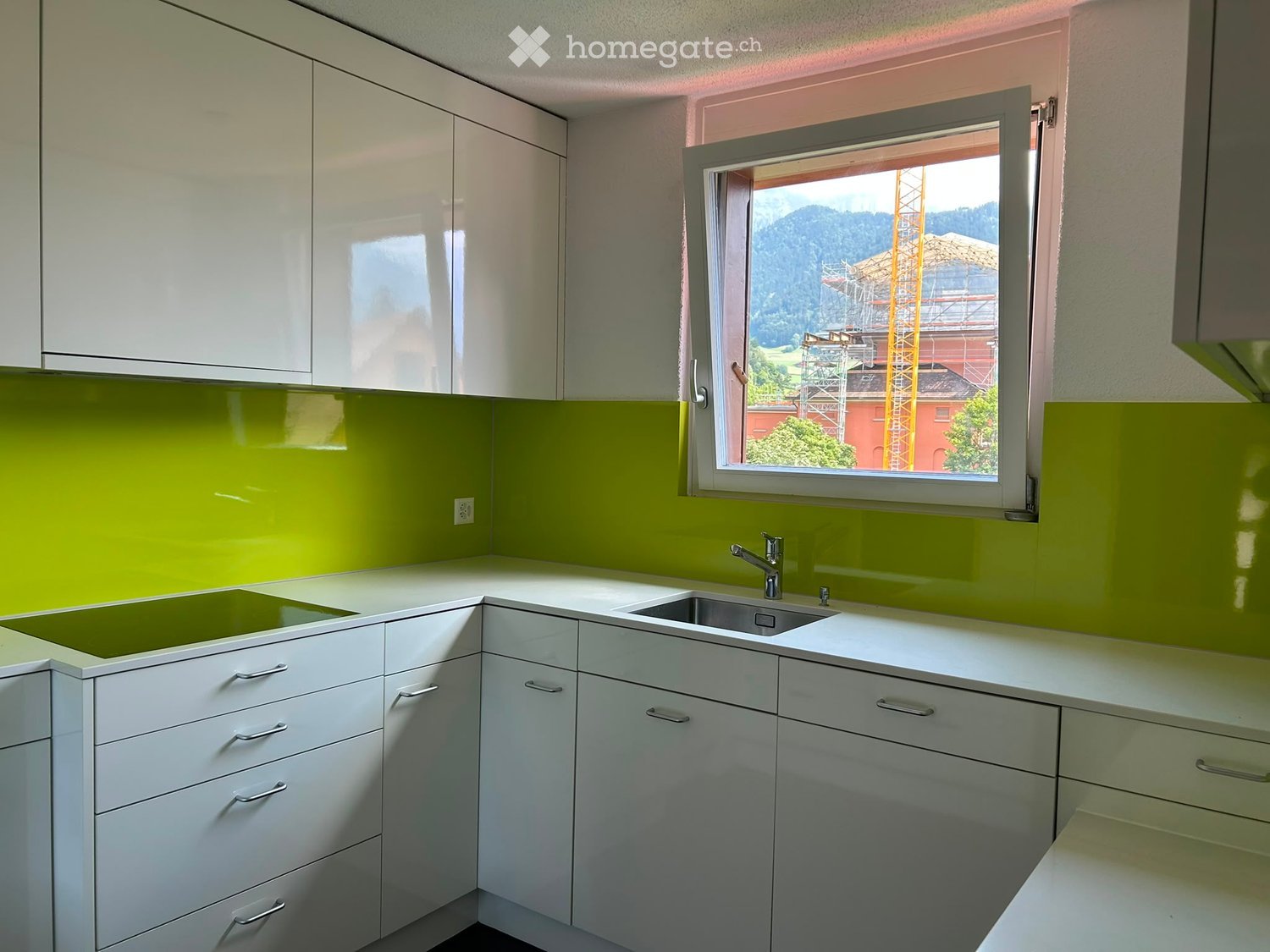 Modern kitchen with white cabinets, green backsplash, and a large window overlooking a scenic view.