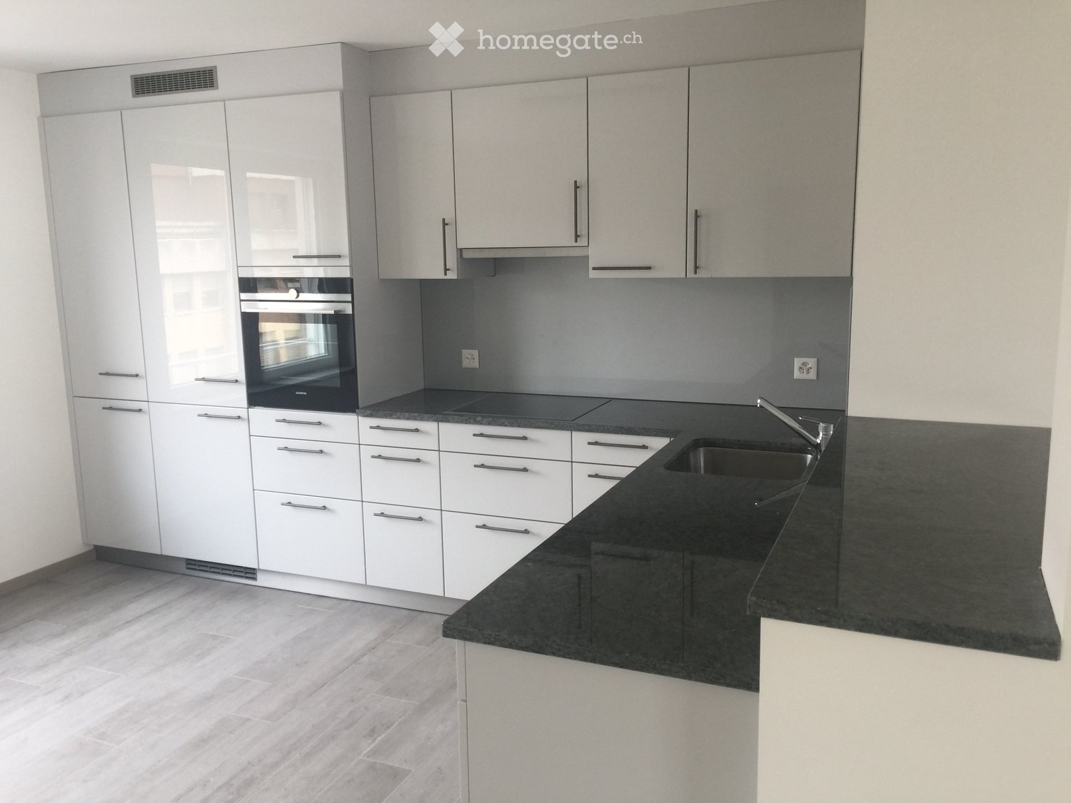 Modern kitchen with white cabinets, black countertop, sink, and built-in oven.