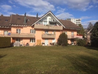 A two-story house with a light pink facade, multiple windows, and a well-maintained lawn in front.