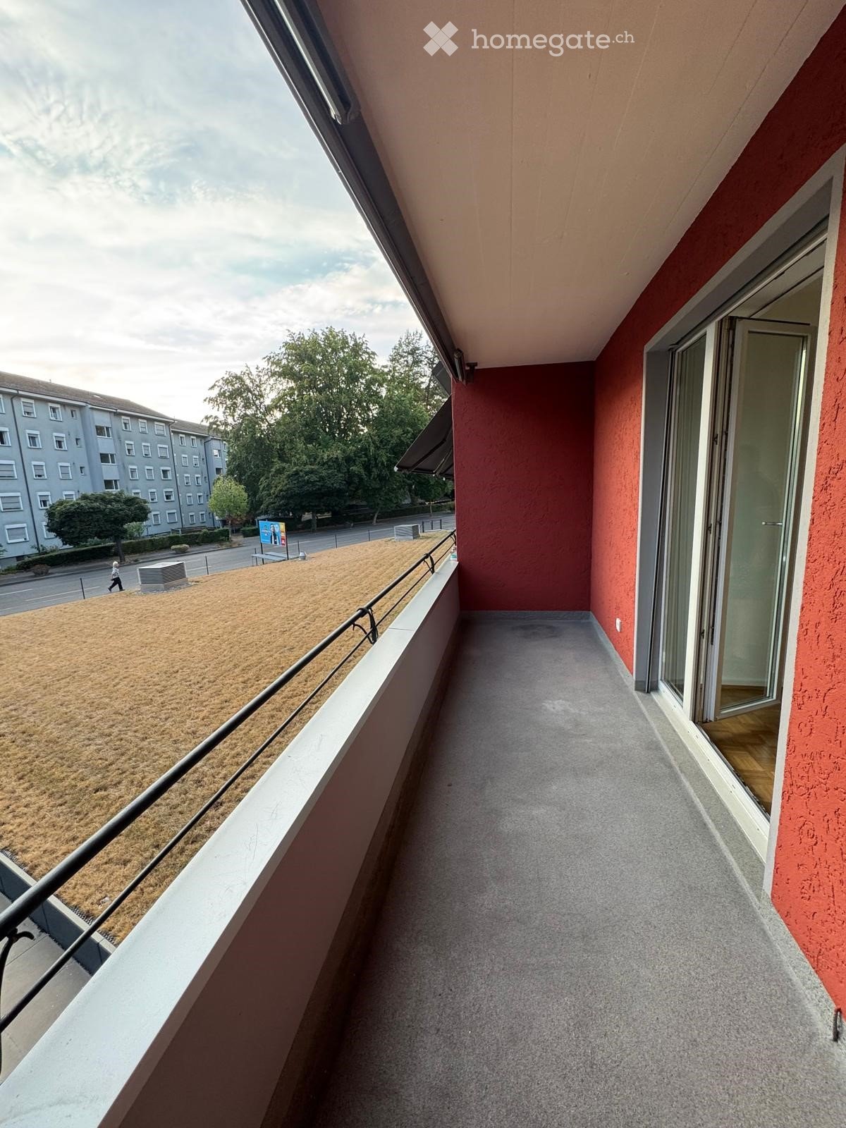 Balcony with grey concrete floor, red walls, metal railing, and large window opening to the interior.