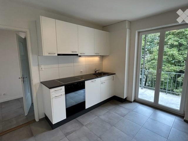 Modern kitchen with white cabinets, black countertop, built-in oven, sink, and a sliding glass door leading to a balcony.