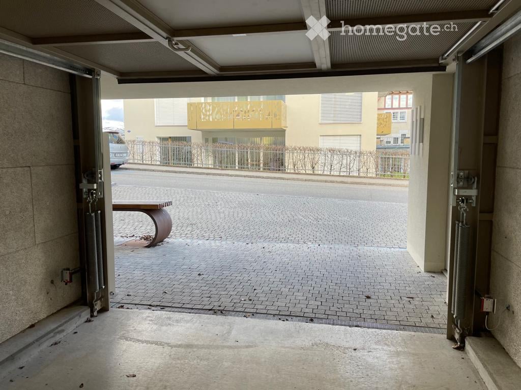 Garage entrance with automated doors, brick-paved floor, and a small bench nearby.