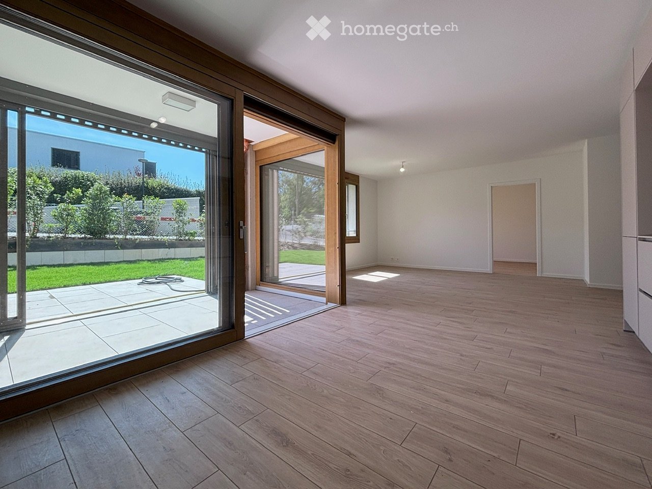 Empty room with wooden flooring, large sliding glass doors leading to a patio, white walls, and minimal lighting.