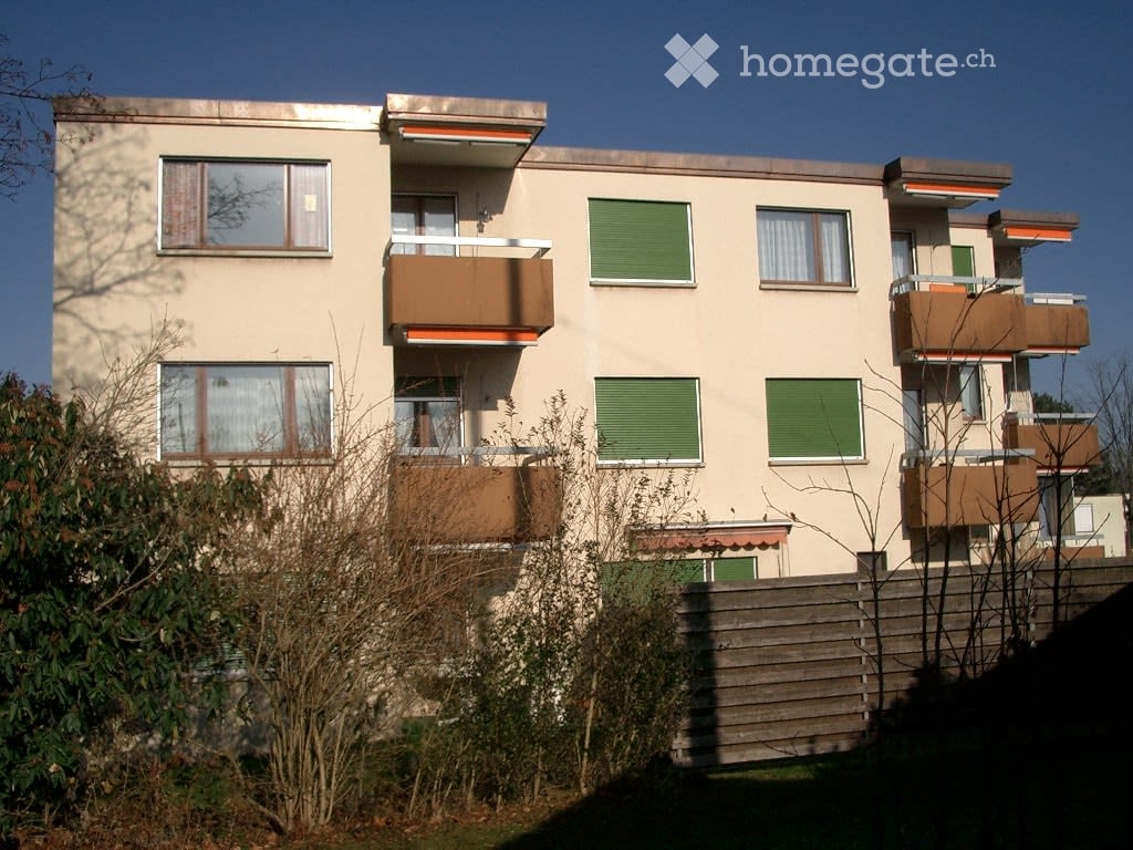 Multi-story building, multiple balconies, beige exterior with brown accents, multiple windows, wooden fence