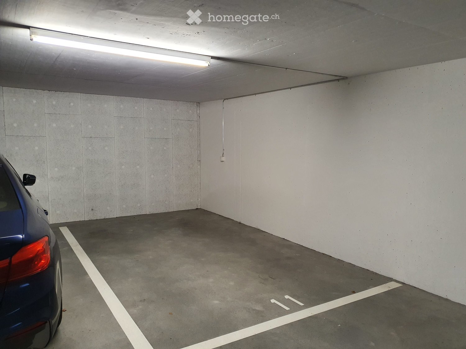 Underground parking space with a single car parked, marked parking spaces, and fluorescent lighting.