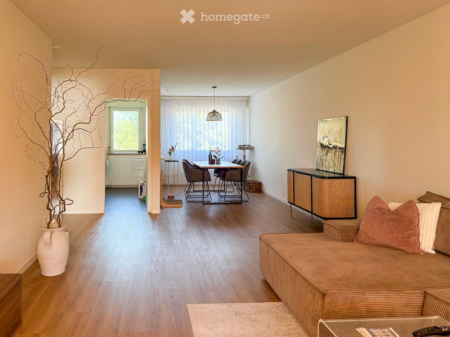 Open-plan living and dining area with a sofa, coffee table, sideboard, dining table, chairs, and decorative vase.