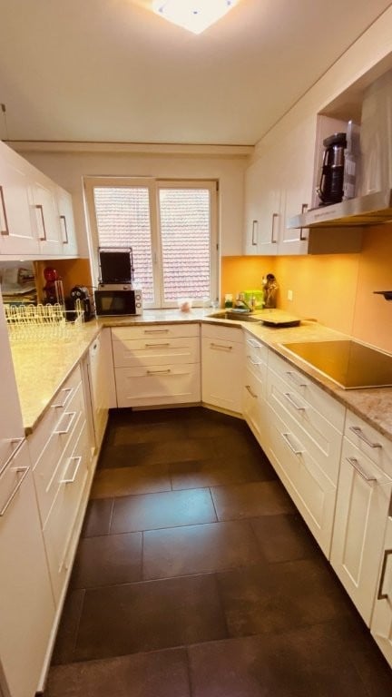 Modern kitchen with white cabinets, dark tiled floor, and stainless steel appliances. Features a microwave, coffee maker, and a sink.