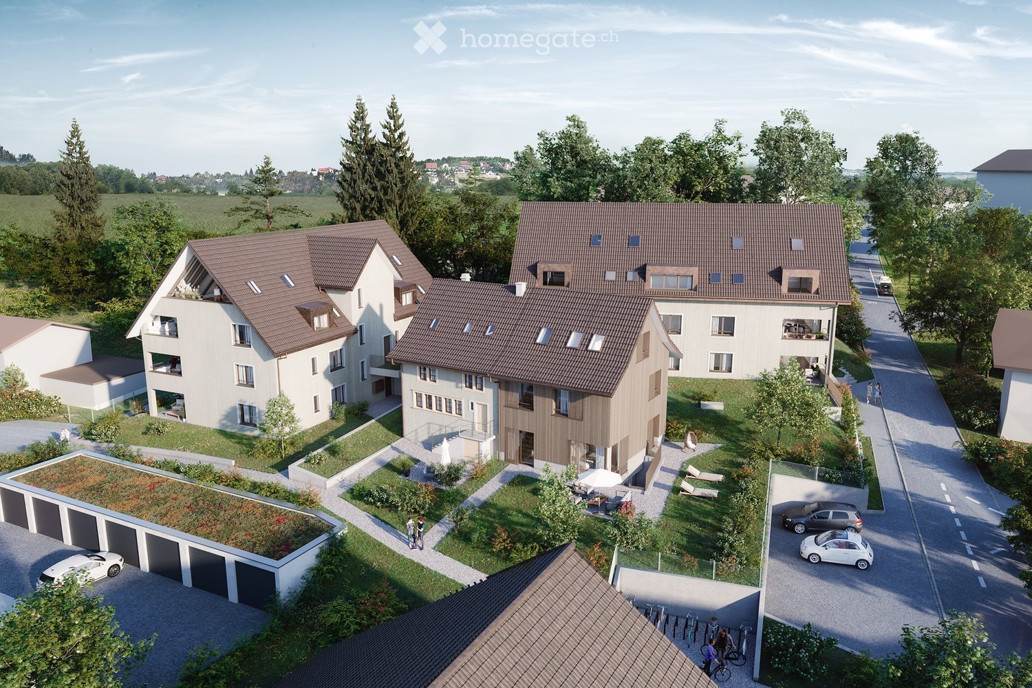 Aerial view of a residential complex with multiple modern houses, garages, and landscaped gardens. The houses feature brown tiled roofs, large windows, and balconies. The area includes a central green space with lounge chairs, a small umbrella, and a few
