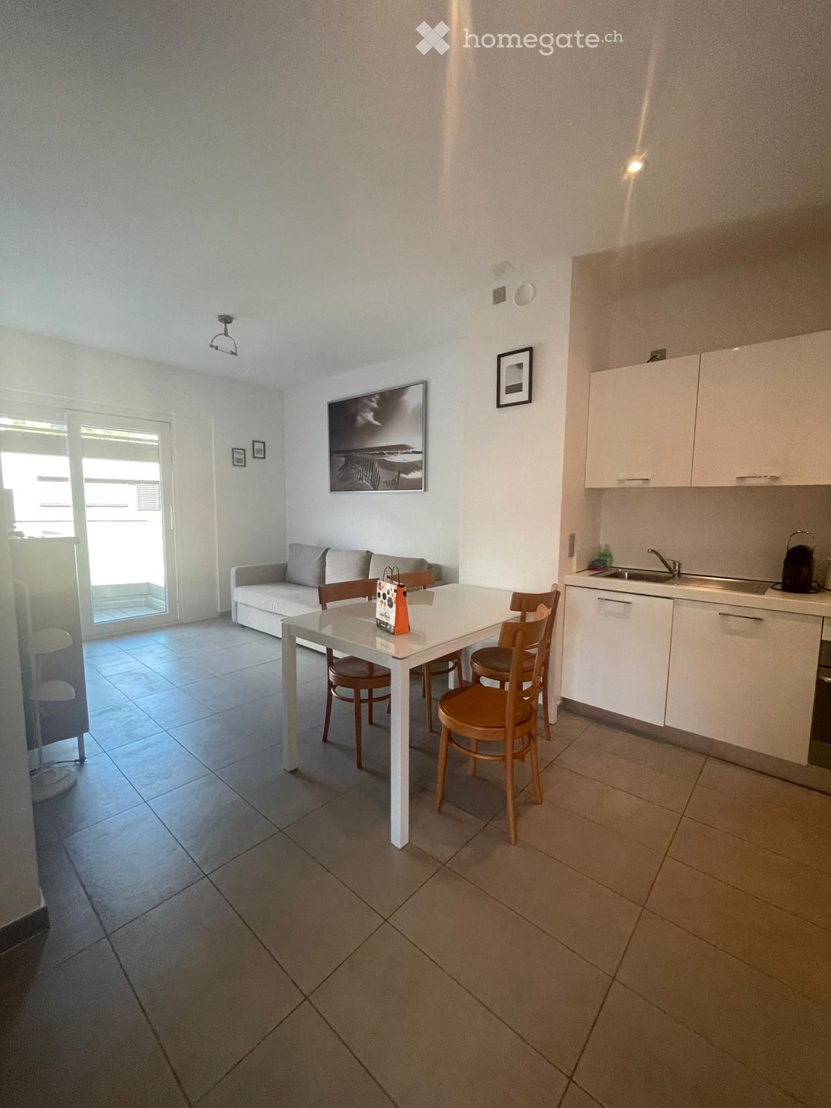 Modern open-plan living and dining area with a sofa, dining table, chairs, and a compact kitchen area with cabinets and a sink.