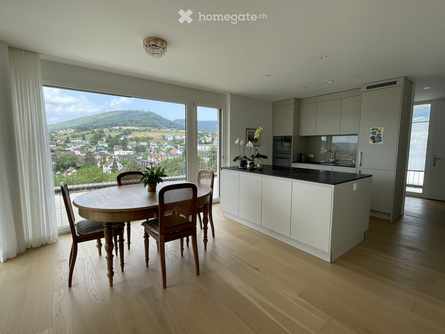 Modern kitchen with white cabinets, black countertop, dining area with wooden table and chairs, large windows offering scenic view.