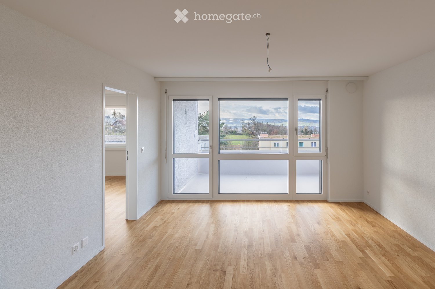 Empty room with wooden flooring, large windows, and white walls. No furniture or equipment present.