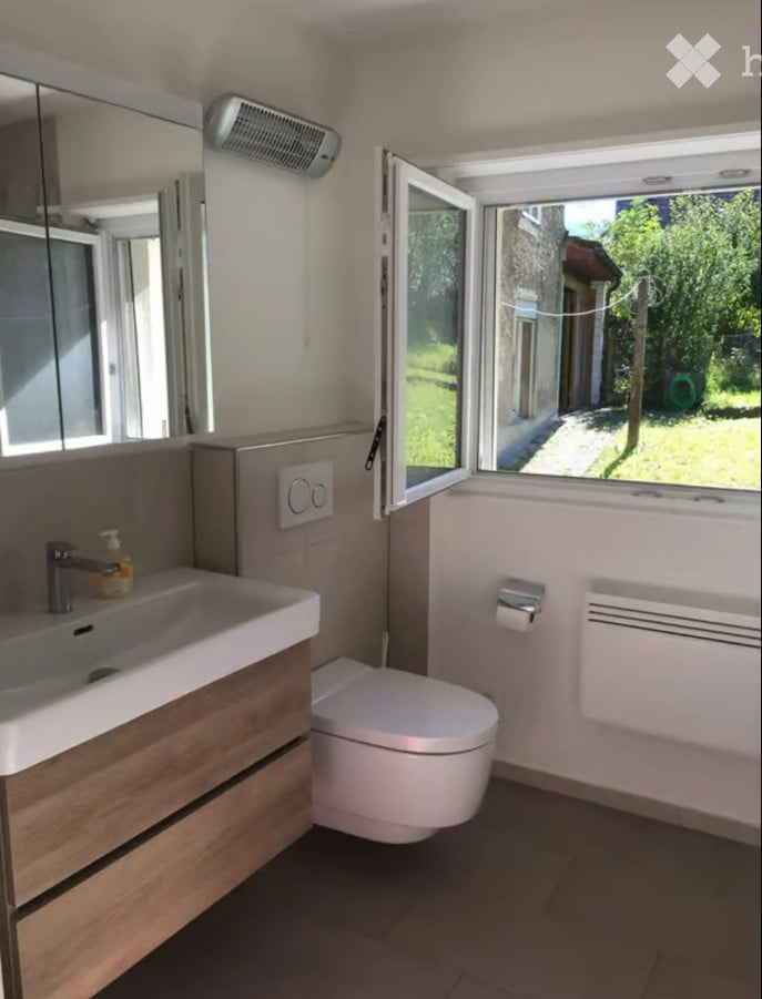 Modern bathroom with a white sink, toilet, mirror, and a window offering a view of the garden.