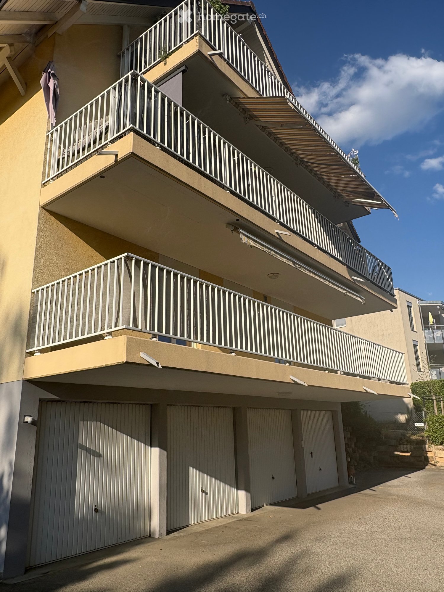 Multi-story residential building with multiple balconies, beige exterior, and garage area.