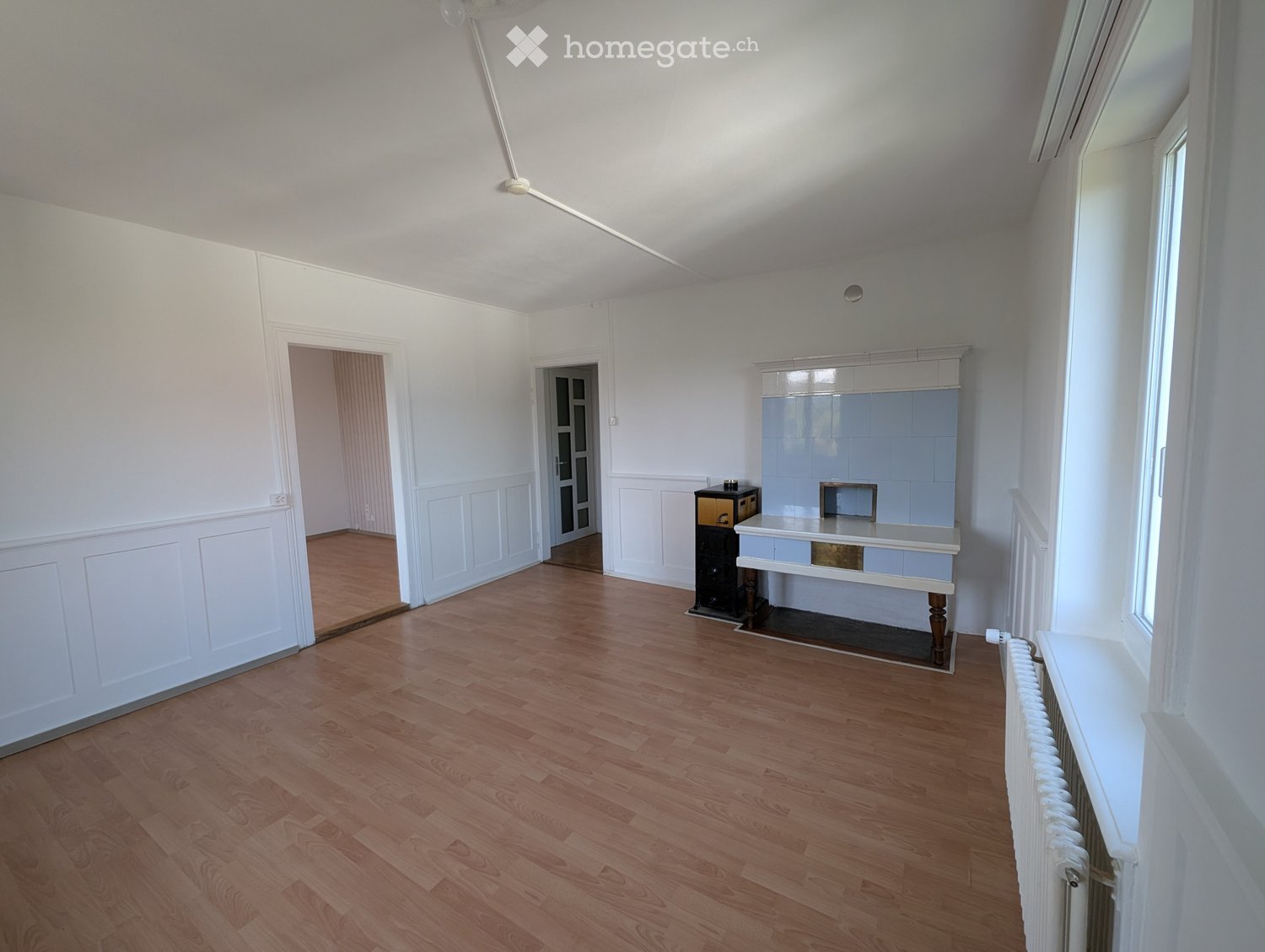 Empty room with wooden flooring, white walls, and a small fireplace area with a bench and small table.
