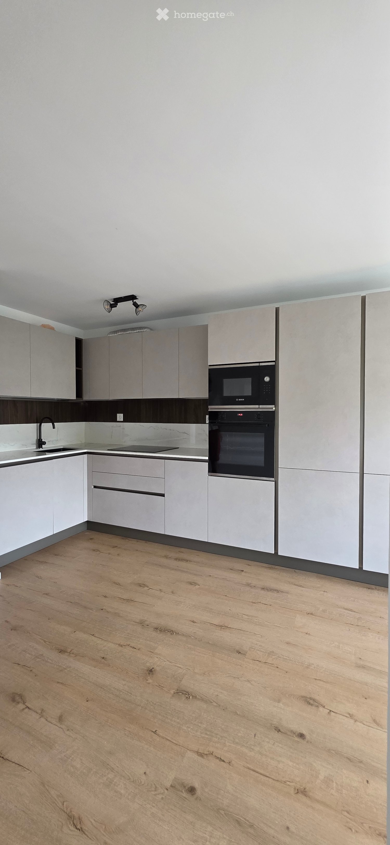 Modern kitchen with light grey cabinets, a microwave, an oven, a sink, and a faucet, featuring a light wooden floor and sleek design.