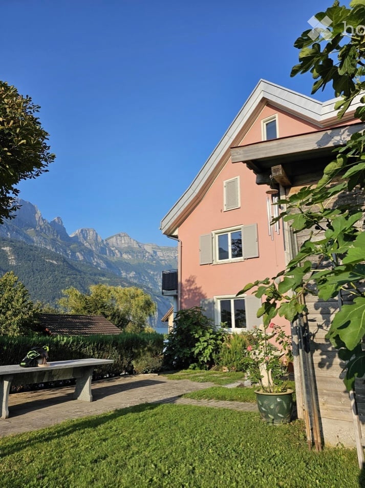pink house, grassy garden, stone bench, potted plants, mountains in the background