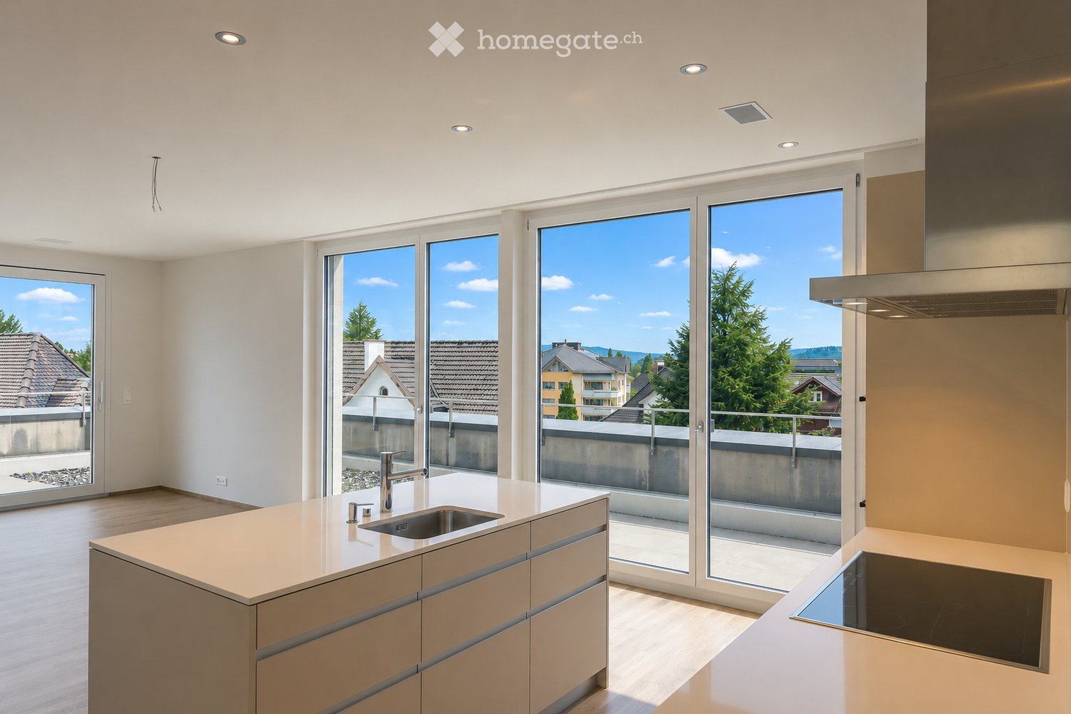 Modern kitchen with light-colored cabinets, a central island with a sink, and large windows offering a view of the surrounding area.
