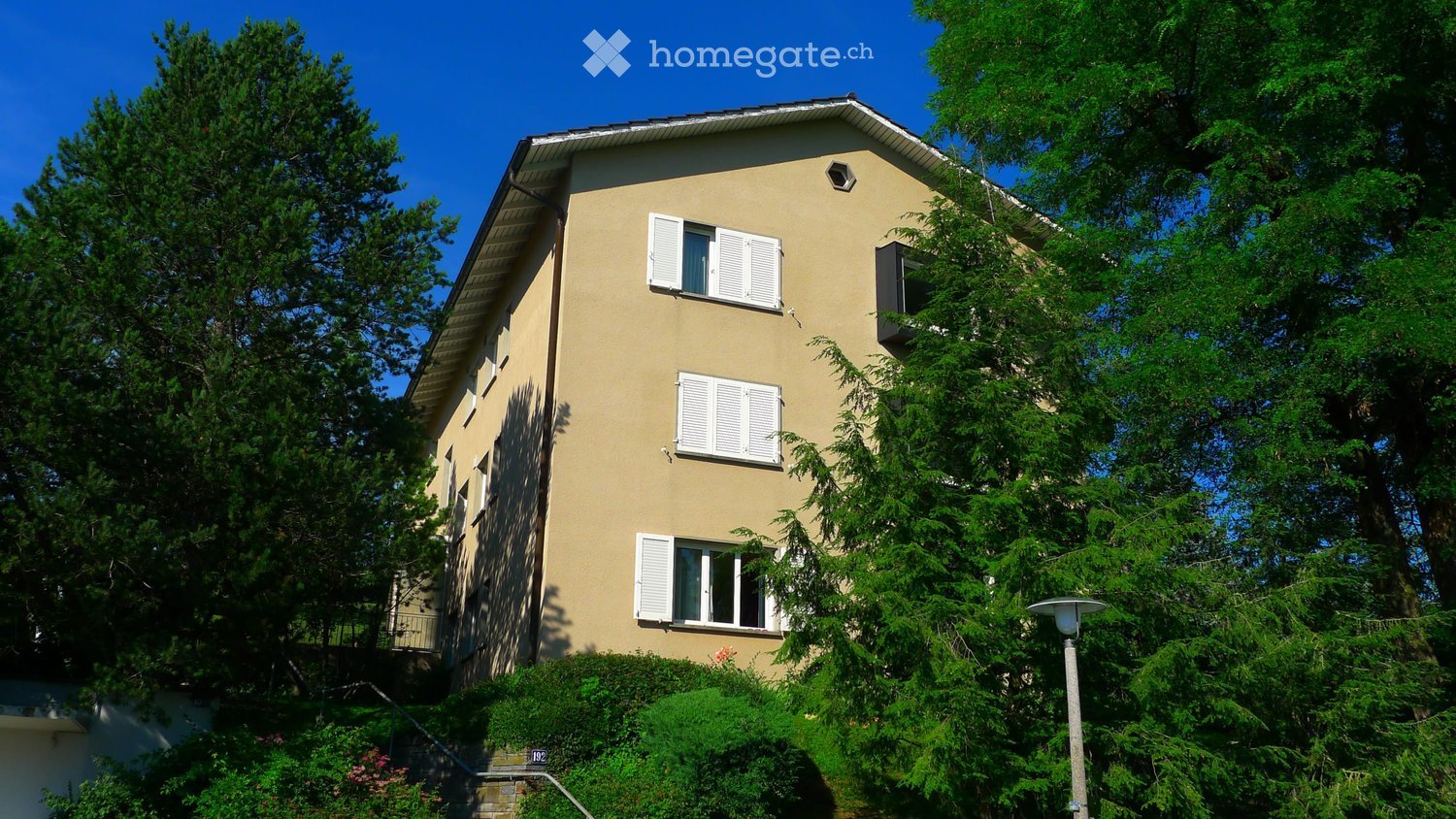3 story house, beige exterior, white shutters, balcony, surrounded by trees