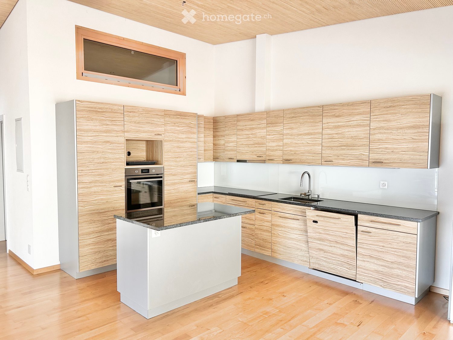 Modern kitchen with light wooden cabinets, granite countertop, and stainless steel appliances including an oven and sink.