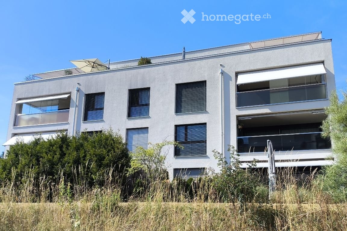 Modern two-story house with white facade, large windows, and multiple balconies. The building features contemporary design with clean lines and is surrounded by greenery.