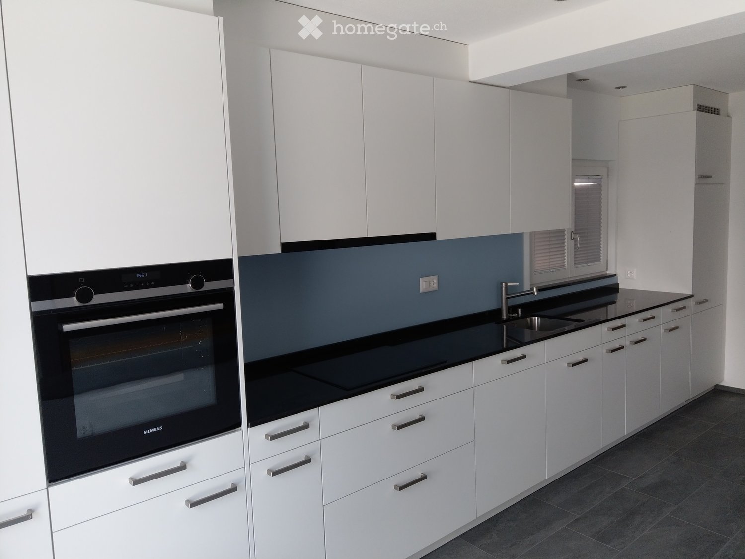 Modern kitchen with white cabinets, black countertops, and stainless steel appliances including an oven and sink.