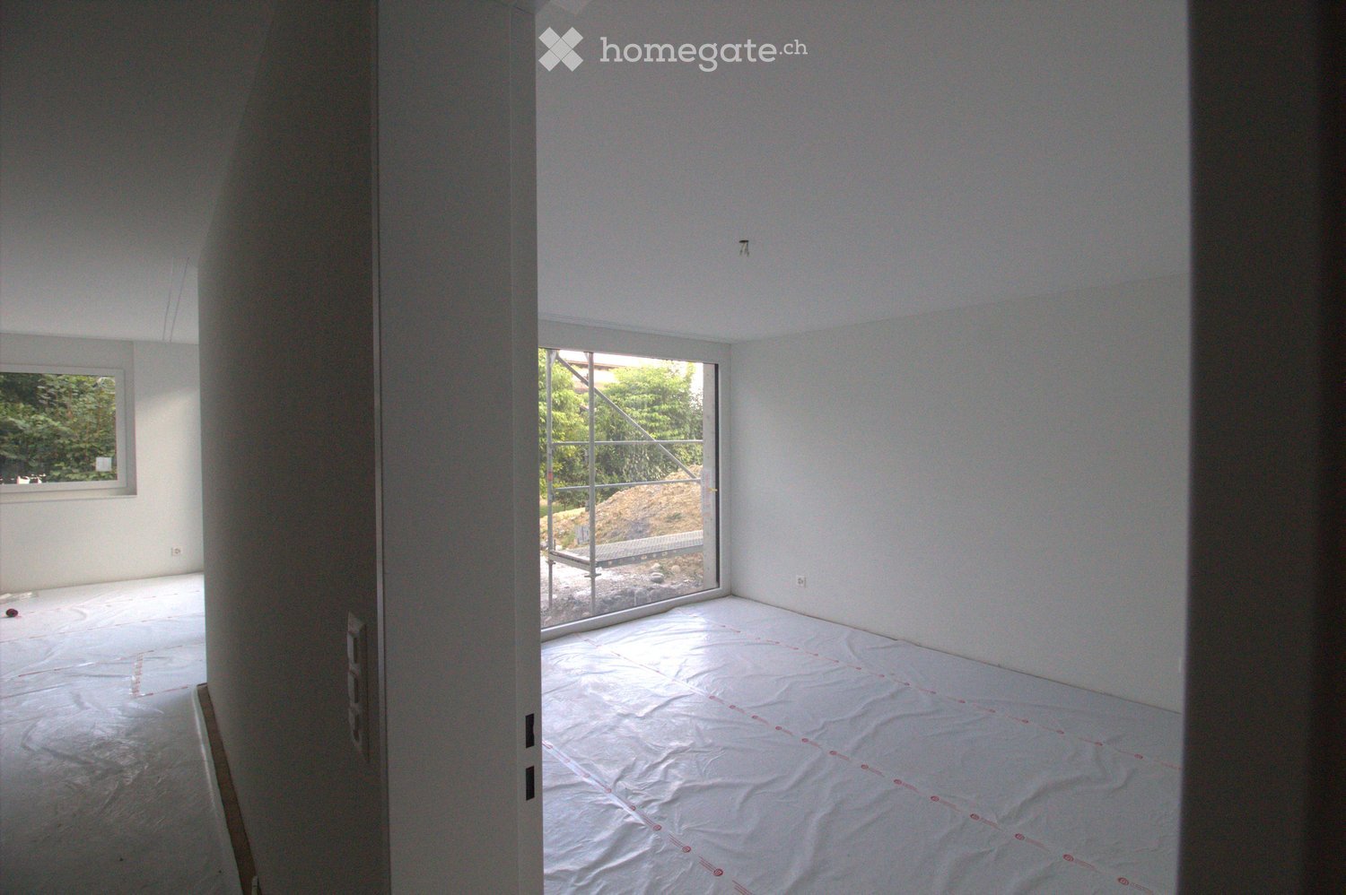 Empty room with white walls, a large window, and a protective plastic sheet on the floor.