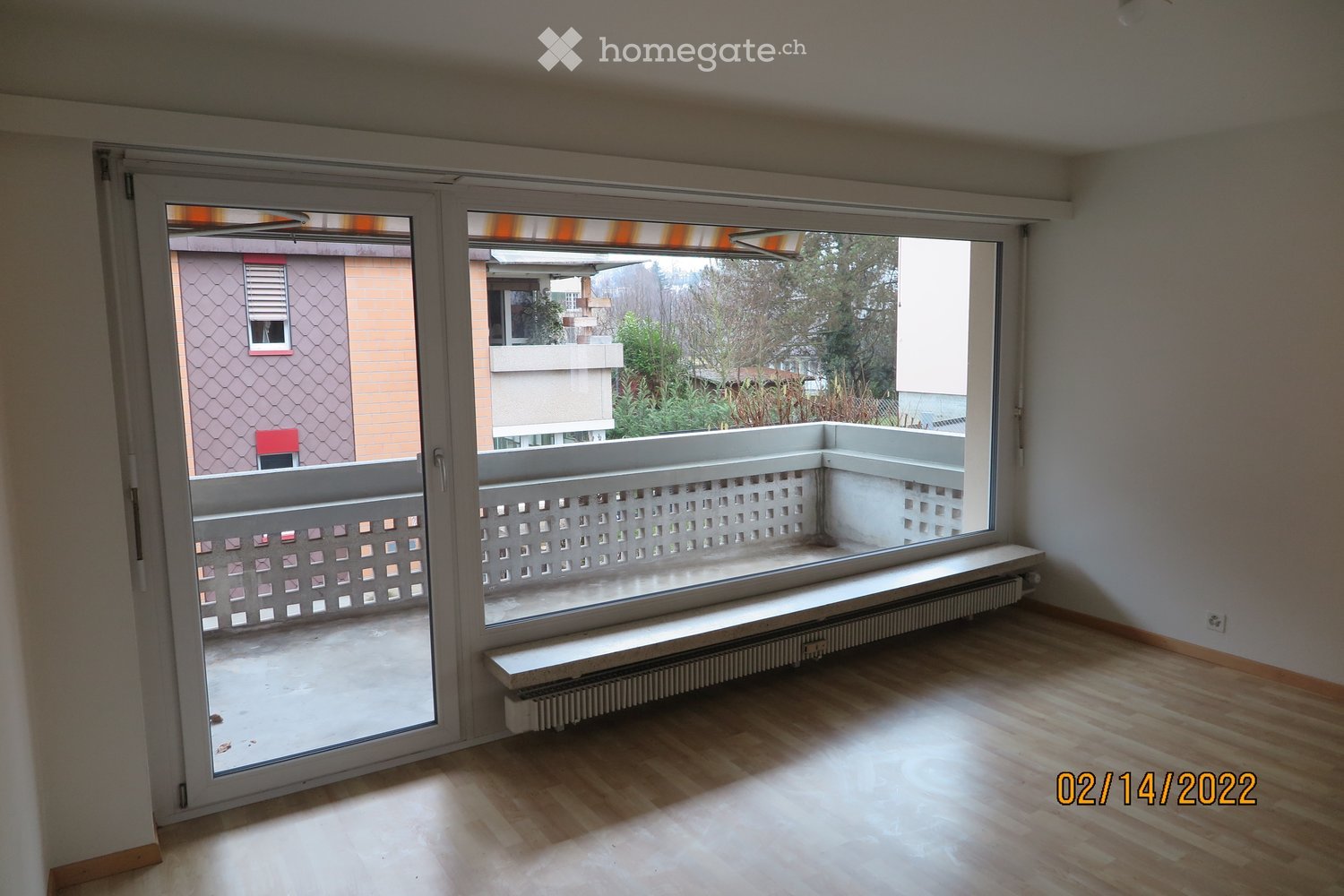Empty room with wooden flooring, large windows, radiator, and sliding glass doors leading to a balcony.