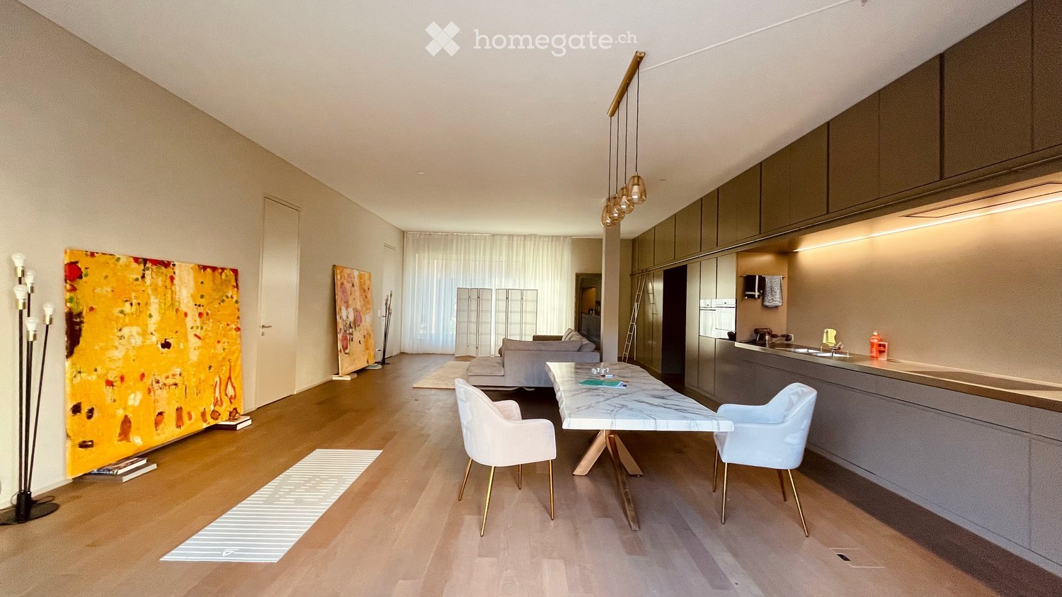 Open-plan living and dining area with modern furniture, a sleek kitchen, and large windows with curtains.