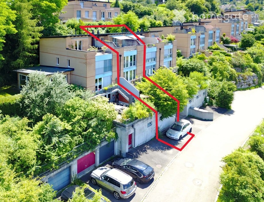 Aerial view of a multi-story residential building with a parking area and surrounding greenery.