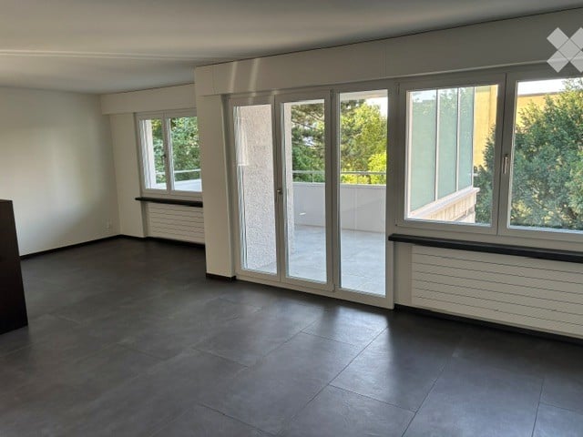 Empty room with dark tiled floor, large windows, and sliding glass doors leading to a balcony.