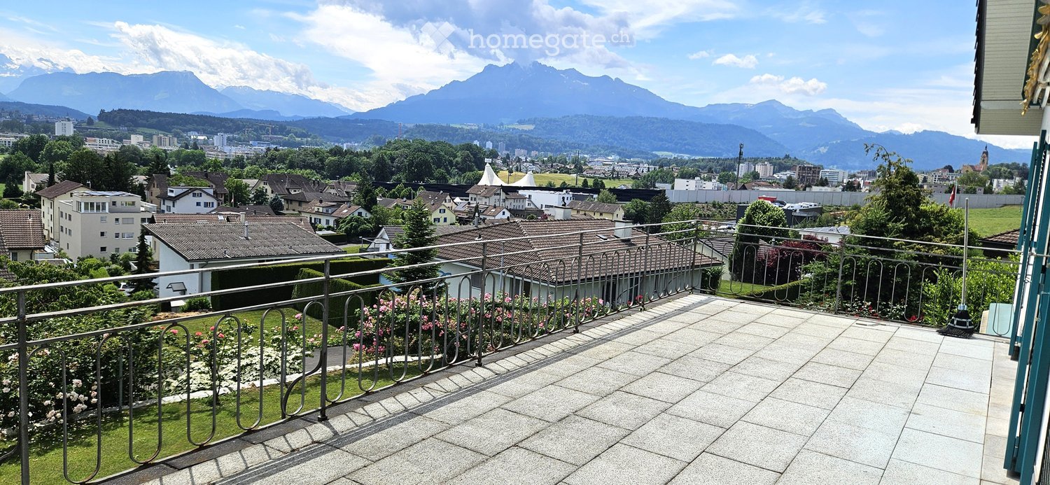 Balcony with metal railing, tiled floor, and a view of a cityscape and mountains in the background.