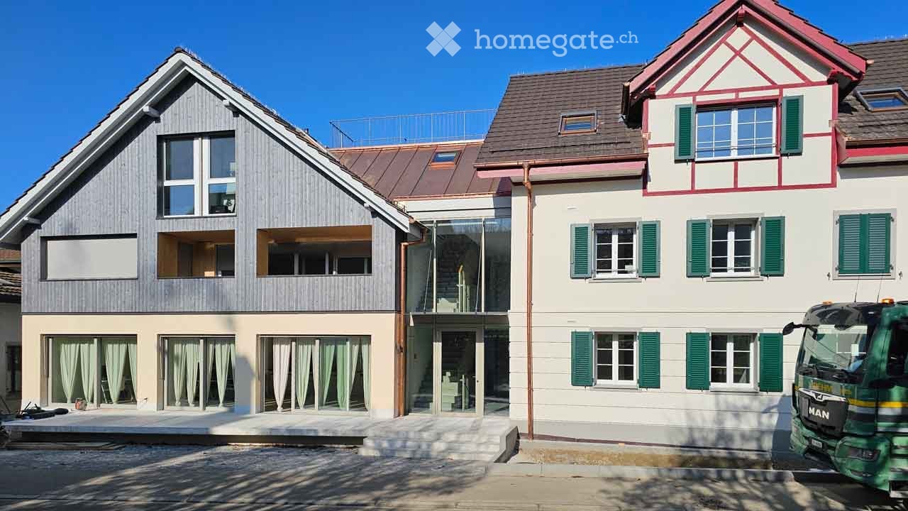 Two-story house with modern and traditional elements, featuring a mix of wooden siding, white walls, green shutters, and a balcony on the upper level.