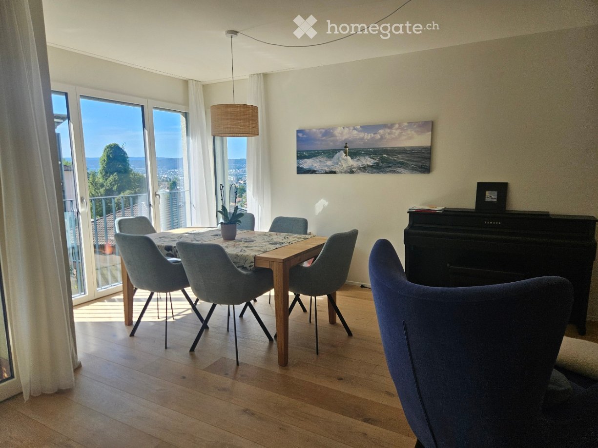 Bright dining area with wooden floor, large windows offering a sea view, dining table with chairs, piano, and a potted plant on the table.
