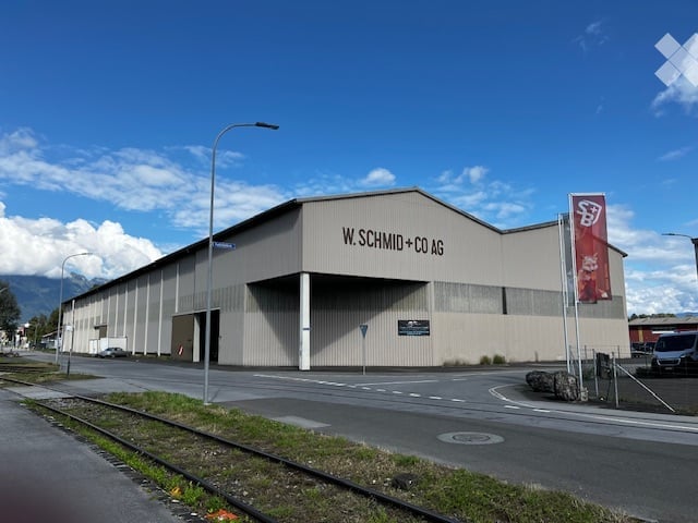 Modern industrial-style building with a large, flat roof and a sign reading "W. SCHMID + CO AG".