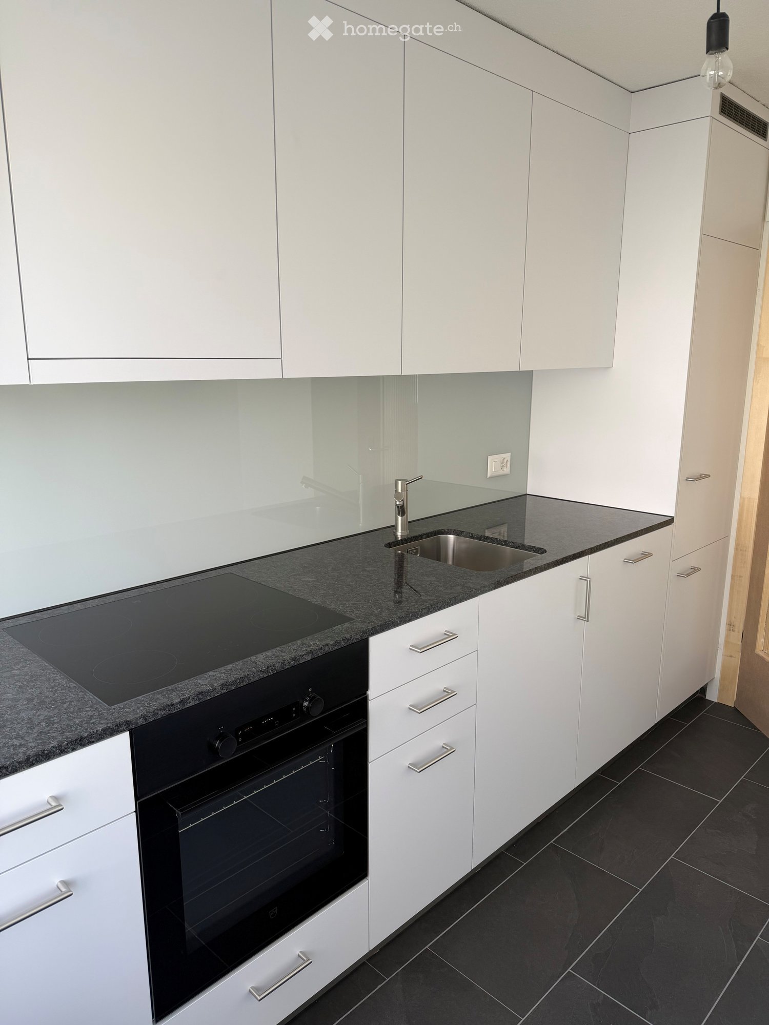 Modern kitchen with white cabinets, black granite countertops, stainless steel sink, induction cooktop, and built-in oven.