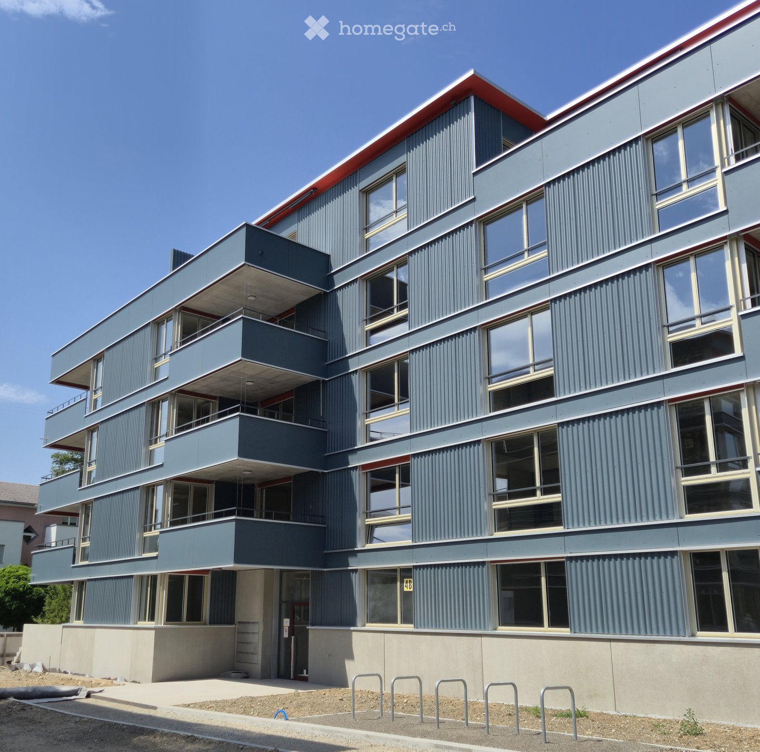 Modern multi-story building with grey and red exterior, large windows, and balconies.