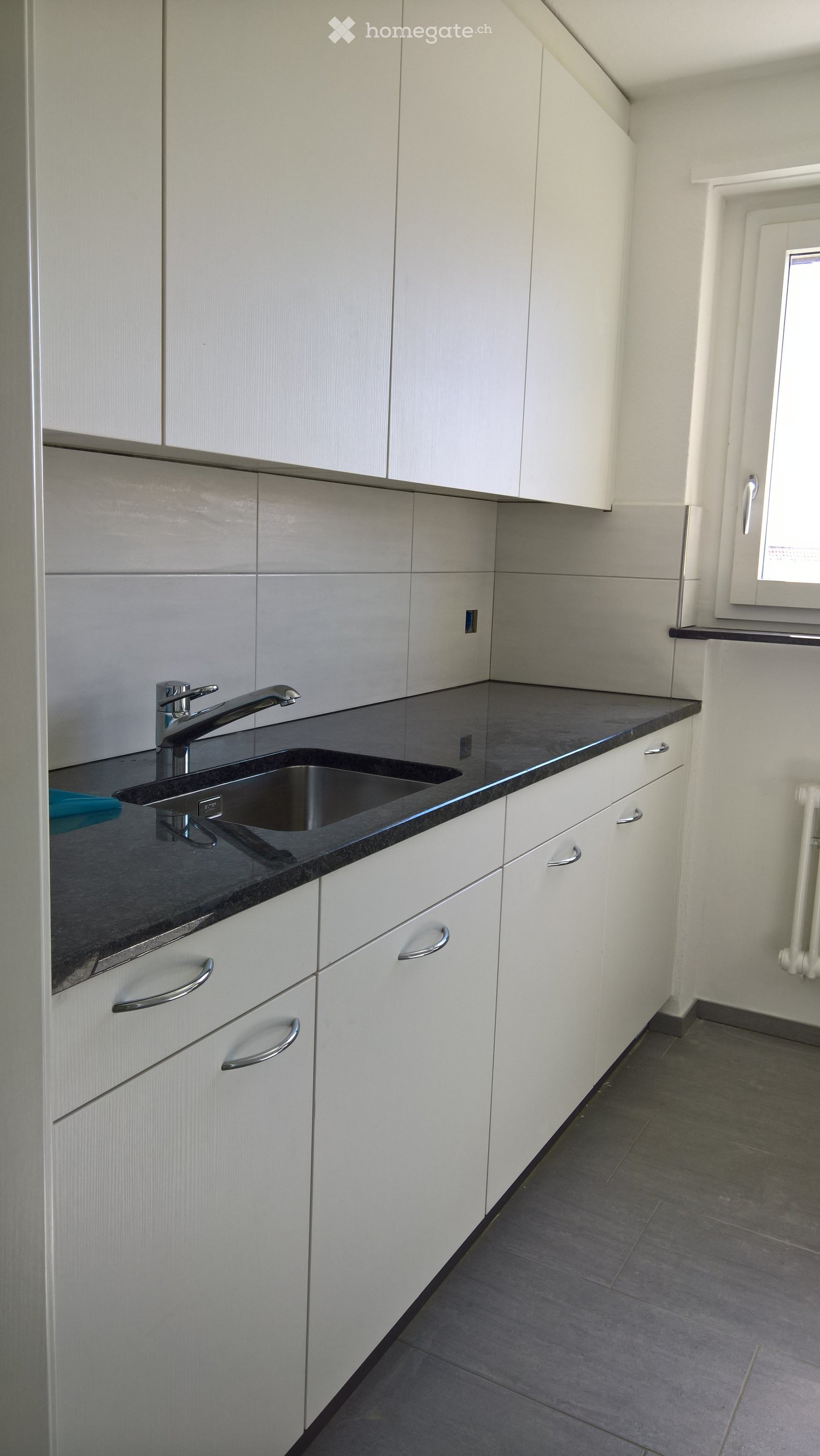 Modern kitchen with white cabinets, dark countertops, and a stainless steel sink.
